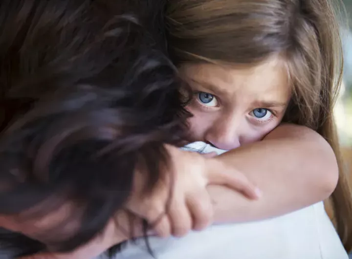 upset little girl looks over mom's shoulder as she gets a hug