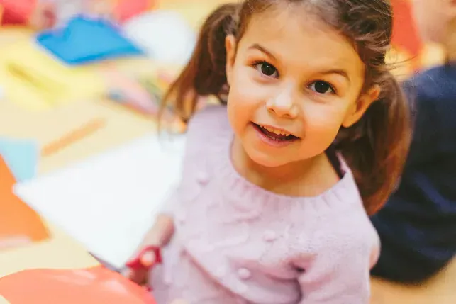 little girl using scissors smiles up at camera