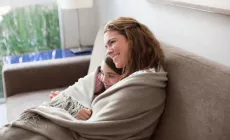 mother and daughter snuggle under blanket while watching TV