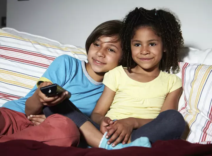 girls sitting on couch, sharing TV remote control 